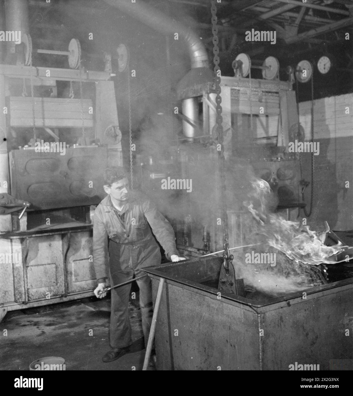 Triebwerksteile werden in dieser Flugzeugmotorfabrik irgendwo in Großbritannien wärmebehandelt. Dieses Verfahren wird als „Ölschwärzung“ bezeichnet, und die Motorkomponenten werden bei 500 °C aus dem Ofen entnommen und dann in Öl getaucht. Das Öl brennt in die Oberfläche des Metalls ein und verhindert Korrosion. Stockfoto