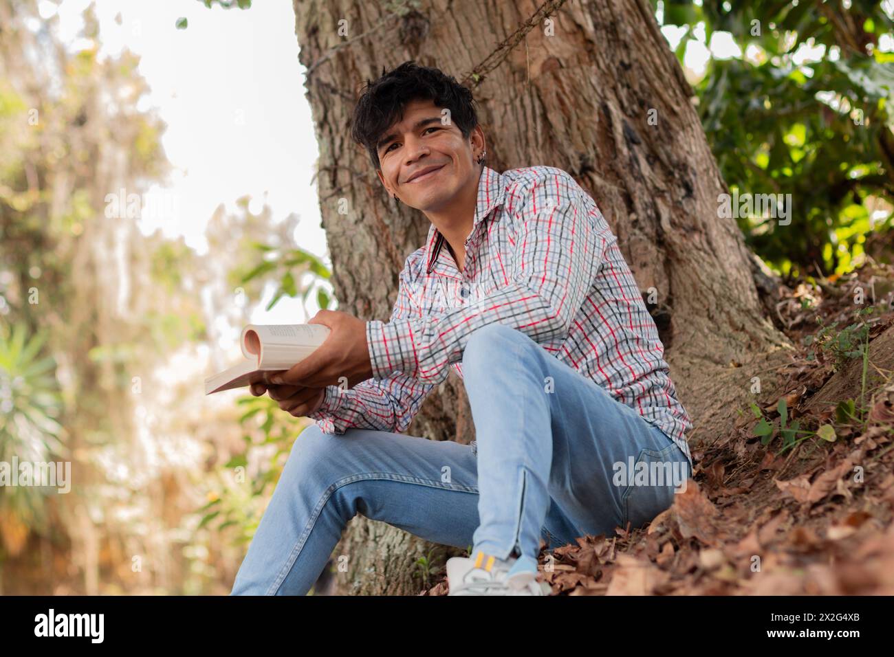 Lifestyle. Junger lateinmann, der unter einem Baum sitzt und ein Buch liest Stockfoto