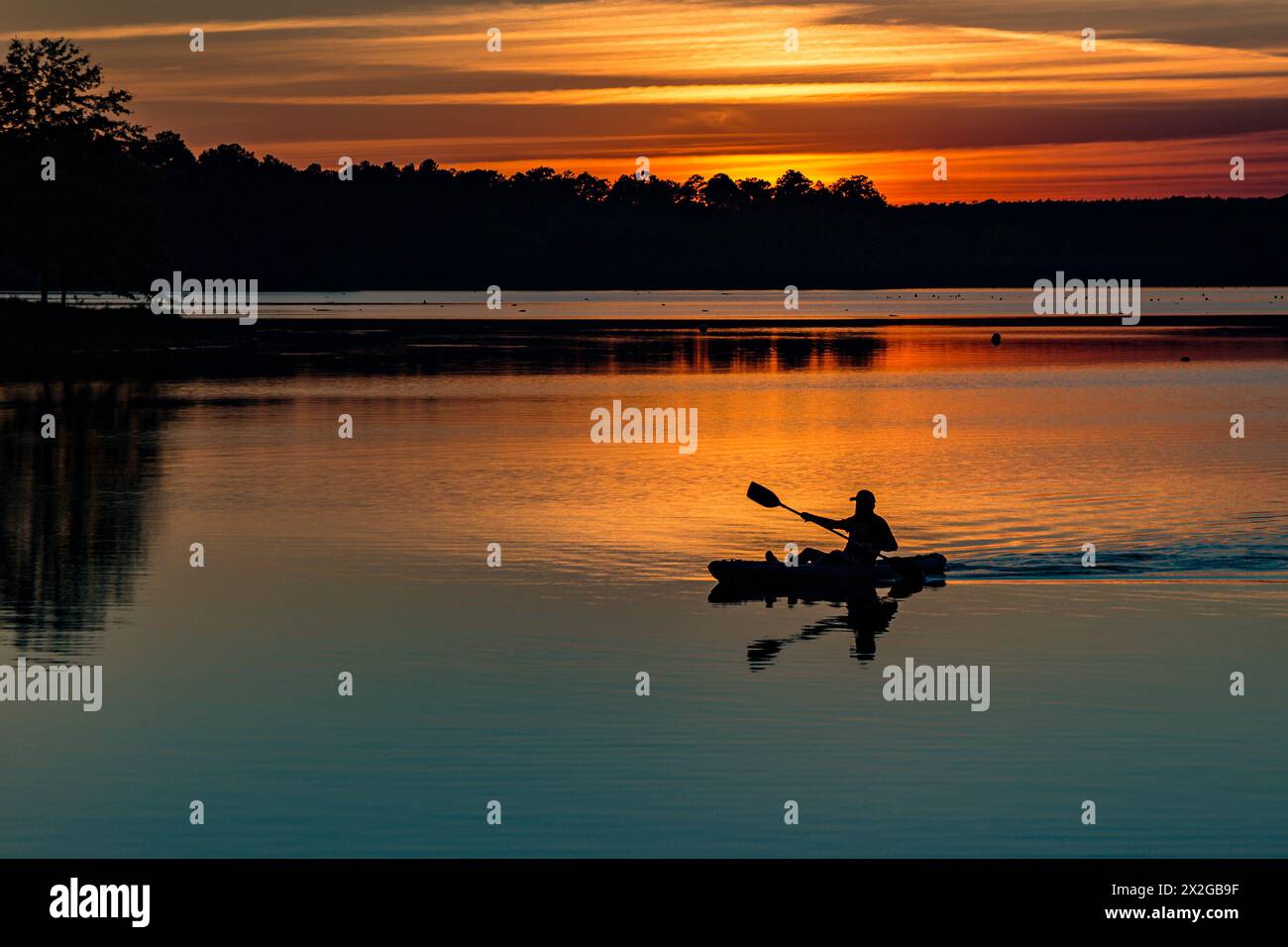 Mann paddelt sein Kajak bei Sonnenuntergang auf dem See auf dem Little Black Creek Campingplatz in der Nähe von Lumberton, Mississippi Stockfoto