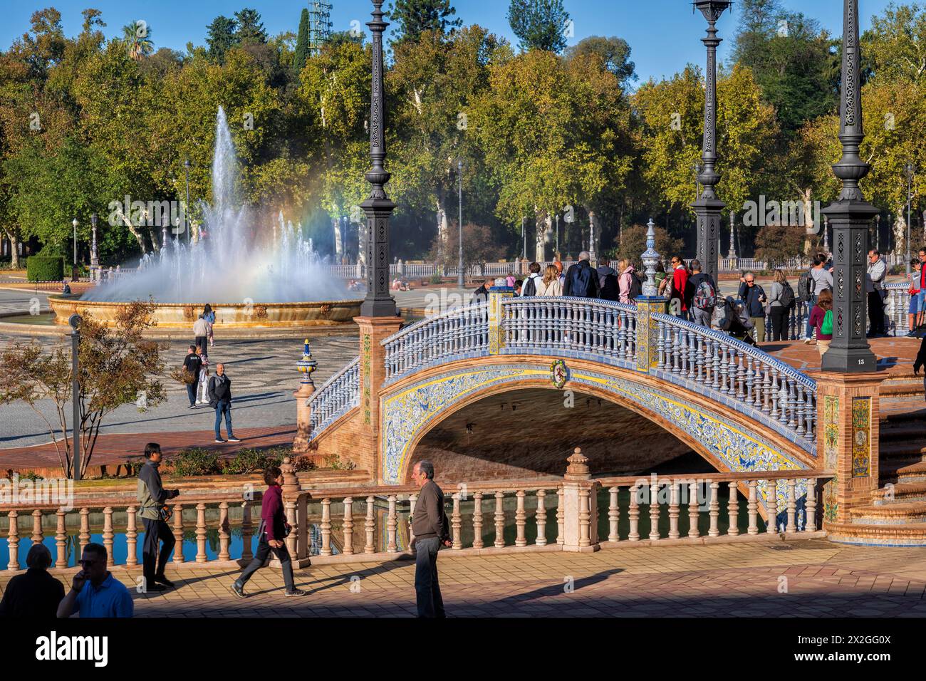 Sevilla, Spanien - 24. Oktober 2023: Menschen an der Plaza de Espana mit Brücke über Kanal und Brunnen im Maria-Luisa-Park, Wahrzeichen der Stadt. Stockfoto