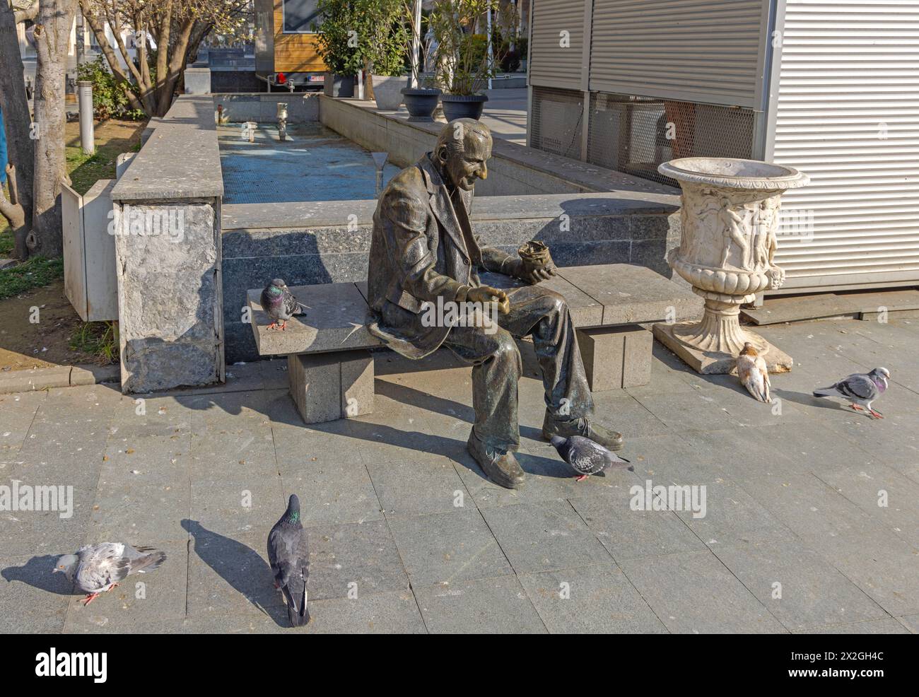 Craiova, Rumänien - 16. März 2024: Bronzestatue des Menschen, der Tauben füttert, sitzt auf der Bank von König Ferdinand und dem Platz der Königin Maria im Stadtzentrum von Sp Stockfoto