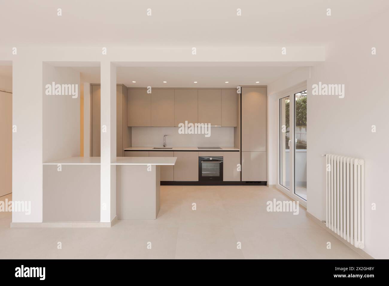Innenausstattung einer modernen beigefarbenen Küche mit einem Arbeitstisch vorne. Die Decke ist weiß und rechts ein großes Fenster. Stockfoto