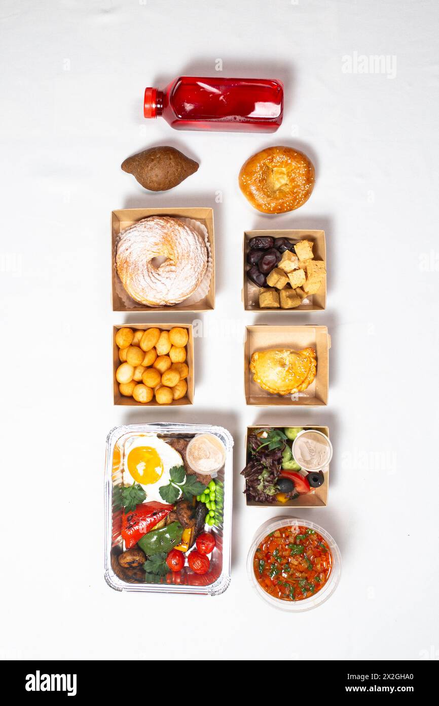 Eine Vielzahl köstlicher Speisen in Behältern auf weißem Hintergrund. Das Essen beinhaltet ein Getränk, Brot, Salat, Suppe und andere Dinge. Stockfoto