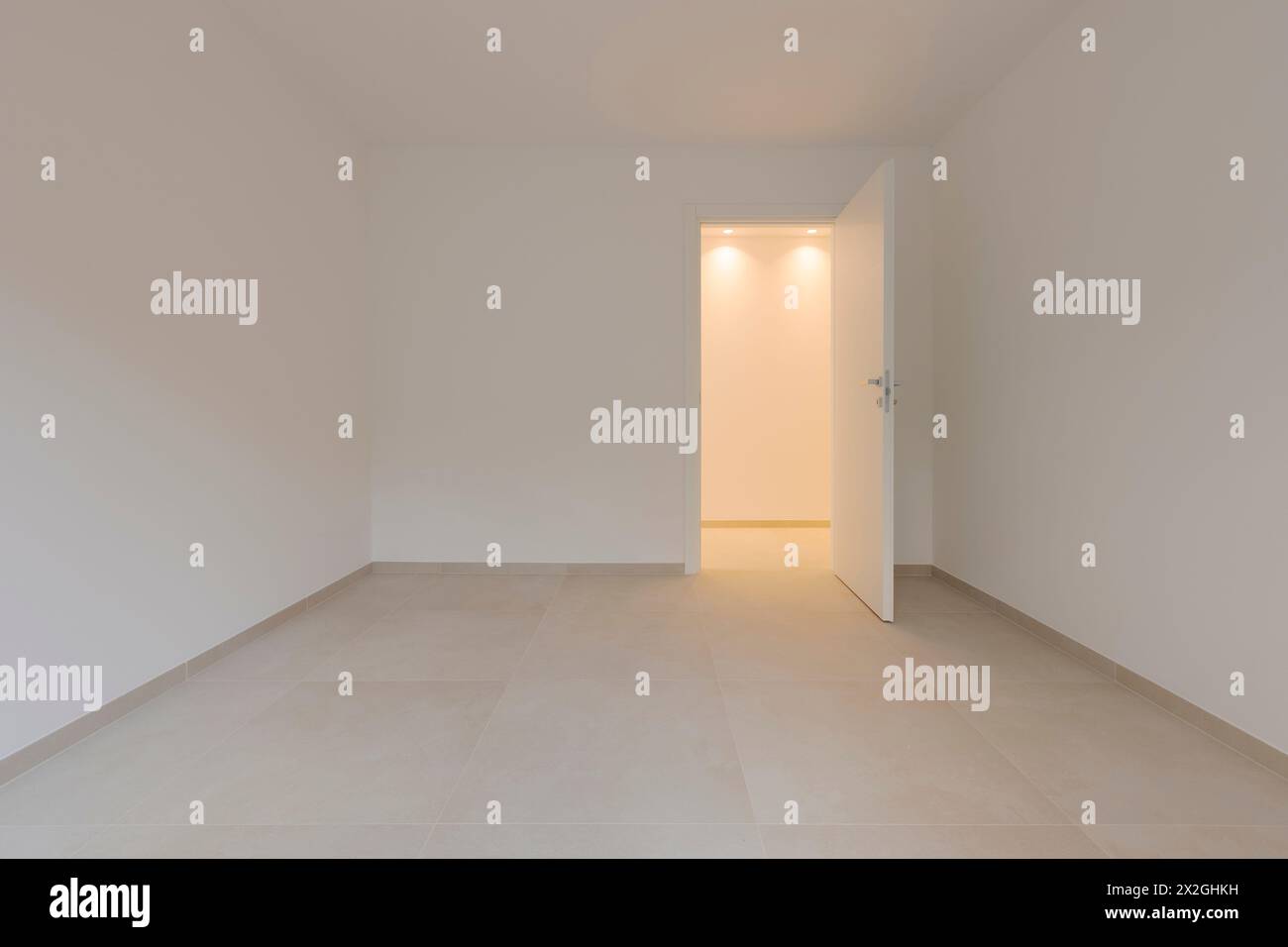 In einem leeren Raum und rechts eine Tür, die zum Flur führt, mit einem Licht an. Alle Wände und Decken sind weiß. Stockfoto