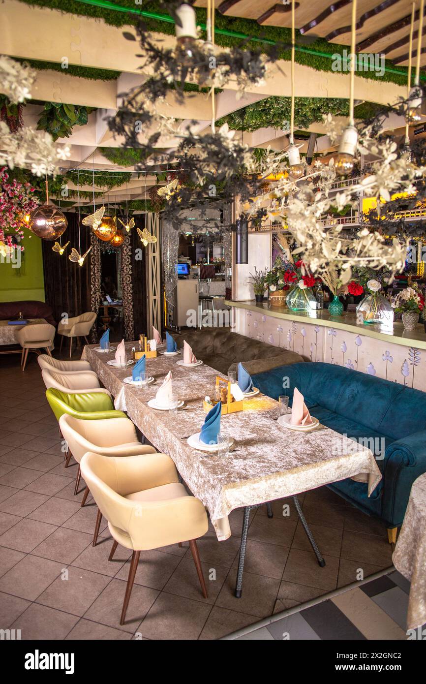 Modernes Restaurant-Design mit Natur-Touch. Grüne Pflanzen, Blumen an Wänden und Decke. Langer Tisch mit Gläsern, Stoffservietten. Stockfoto