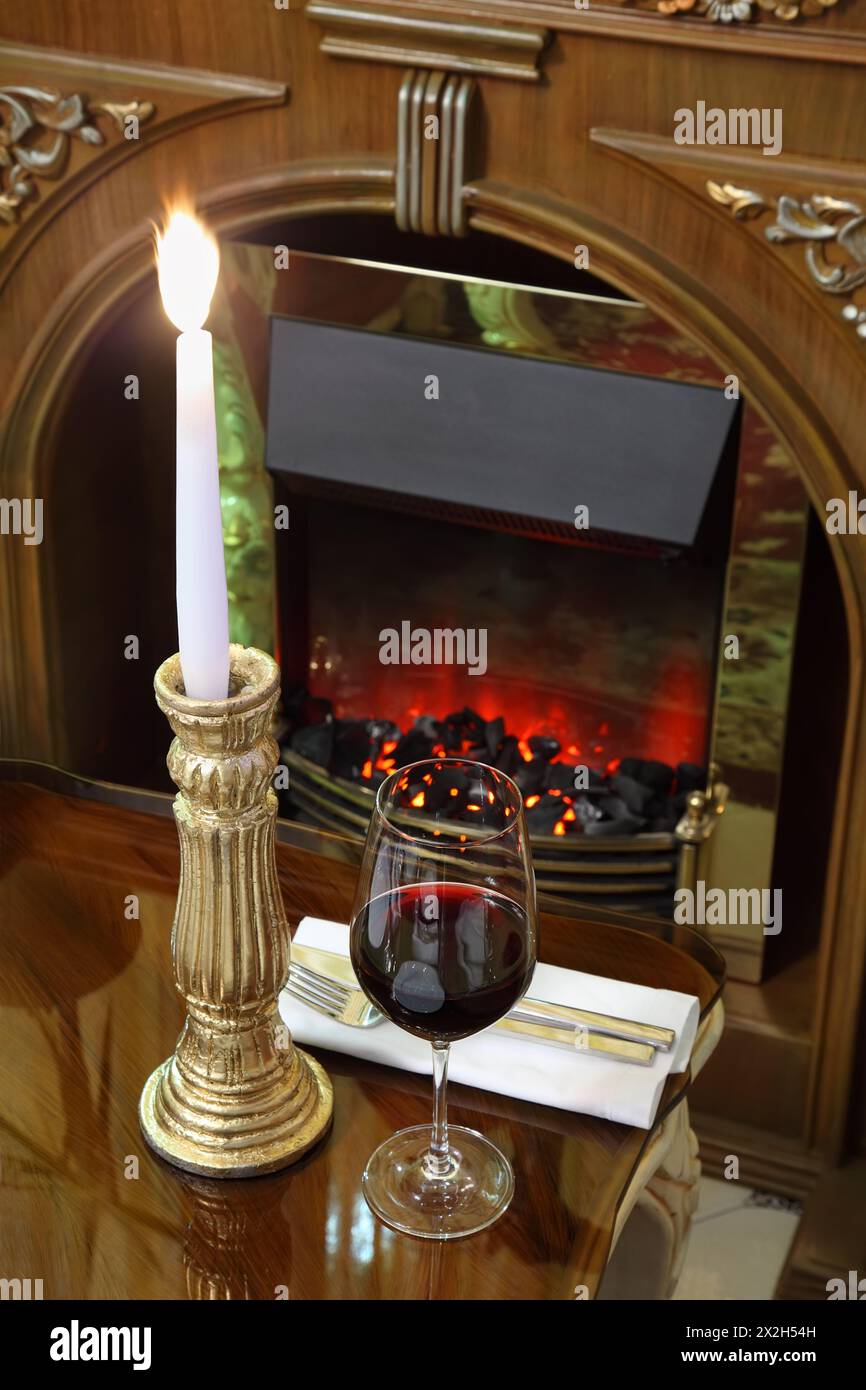 Glas mit Wein und brennender Kerze am Tisch im Restaurant; Kohlen schwelen im Kamin Stockfoto