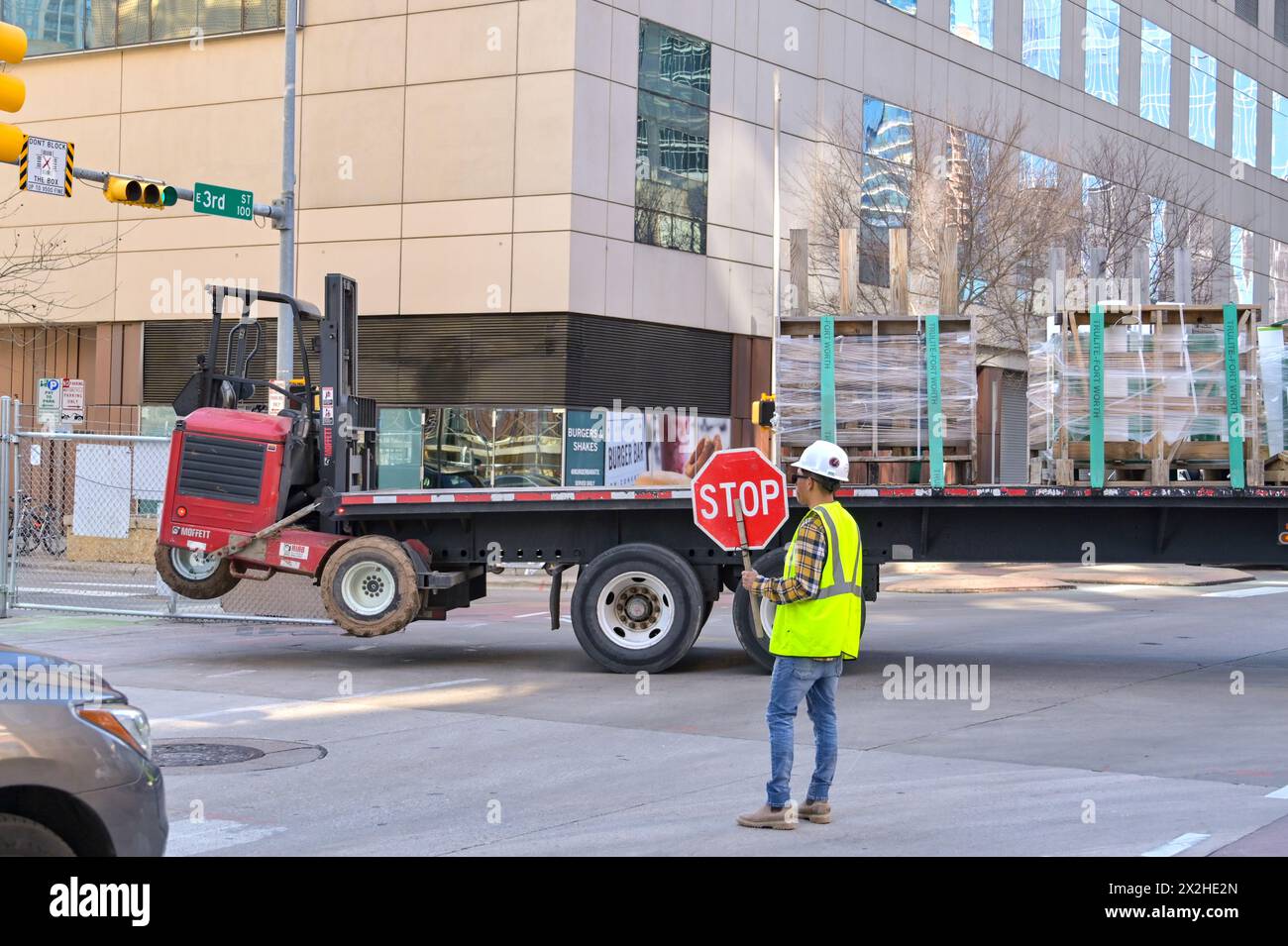 Austin, Texas, USA - 8. Februar 2023: Bauarbeiter mit einem Stoppschild, um den Verkehr zu stoppen, während ein knickgelenkter Lkw auf eine Baustelle zurückfährt Stockfoto