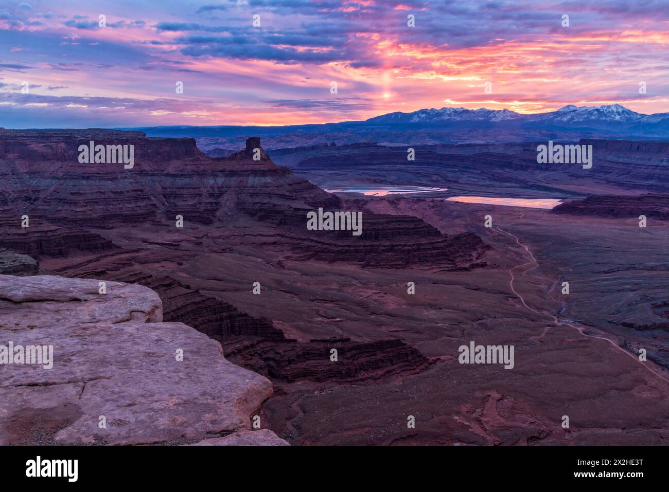 Eine Sonnensäule erleuchtet den Himmel bei Sonnenaufgang hinter den La Sal Mountains, von einem Aussichtspunkt aus gesehen, nahe Moab, Utah. Stockfoto