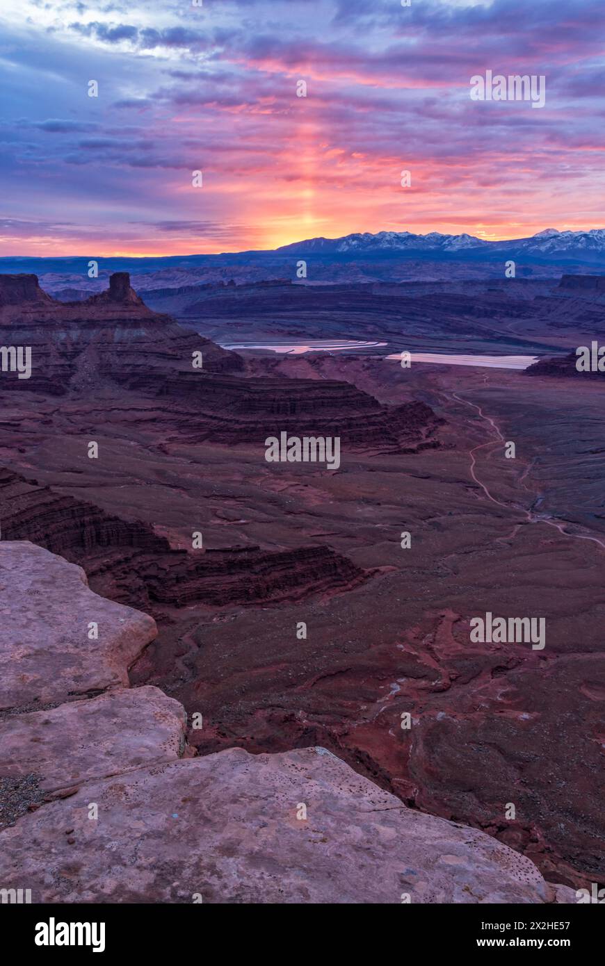 Eine Sonnensäule erleuchtet den Himmel bei Sonnenaufgang hinter den La Sal Mountains, vom Aussichtspunkt Dead Horse Point aus gesehen, in der Nähe von Moab, Utah. Stockfoto