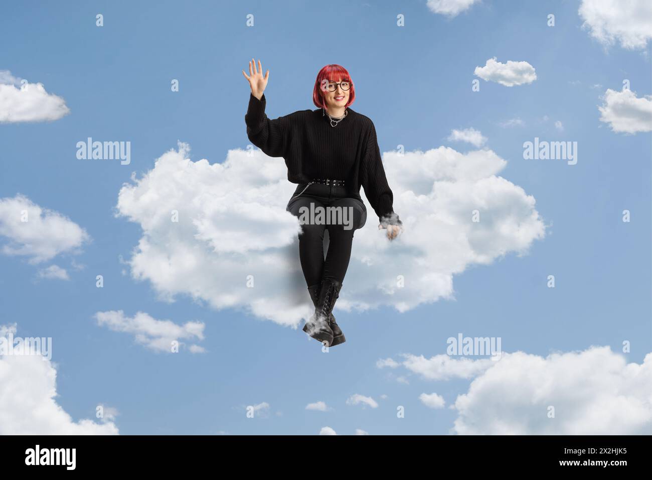 Frau mit rotem Haar, die auf einer Wolke sitzt, ein Buch hält und am Himmel winkt Stockfoto