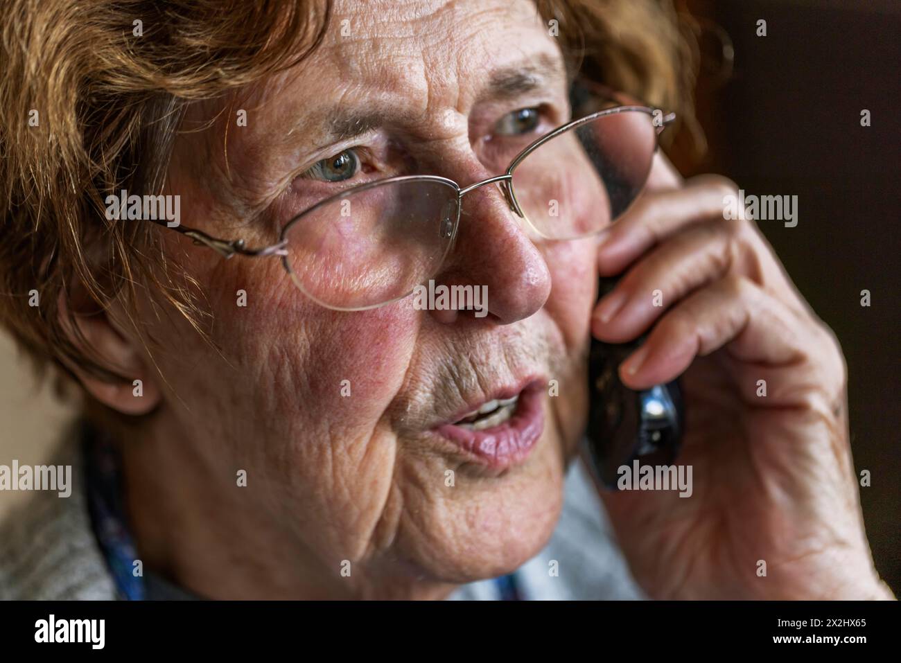 Die Seniorin sieht ernst aus, verängstigt, während sie am Telefon in ihrem Wohnzimmer in Köln, Nordrhein-Westfalen, Deutschland spricht Stockfoto