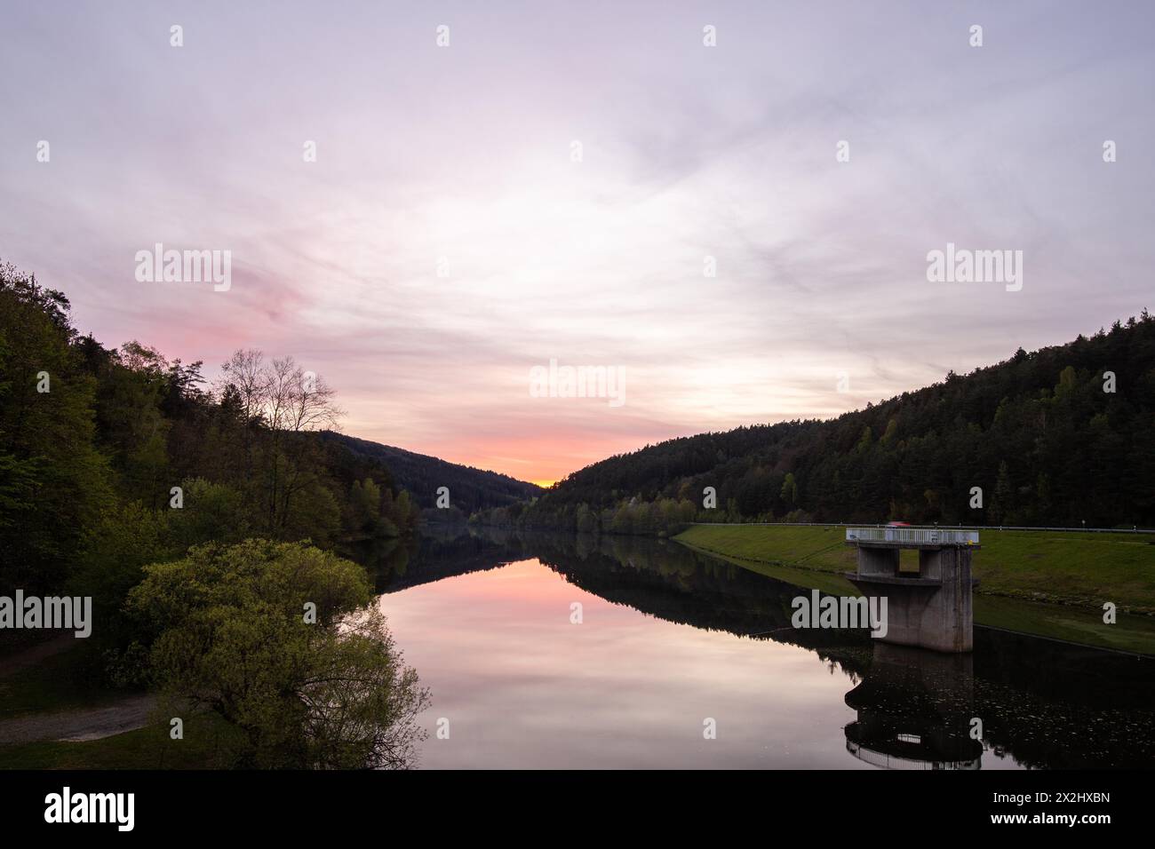 Ein See in einer Landschaftsaufnahme. Ein Sonnenuntergang und die natürliche Umgebung spiegeln sich im Wasser des Stausees wider. Marbach Stausee, Odenwald, Hessen Stockfoto