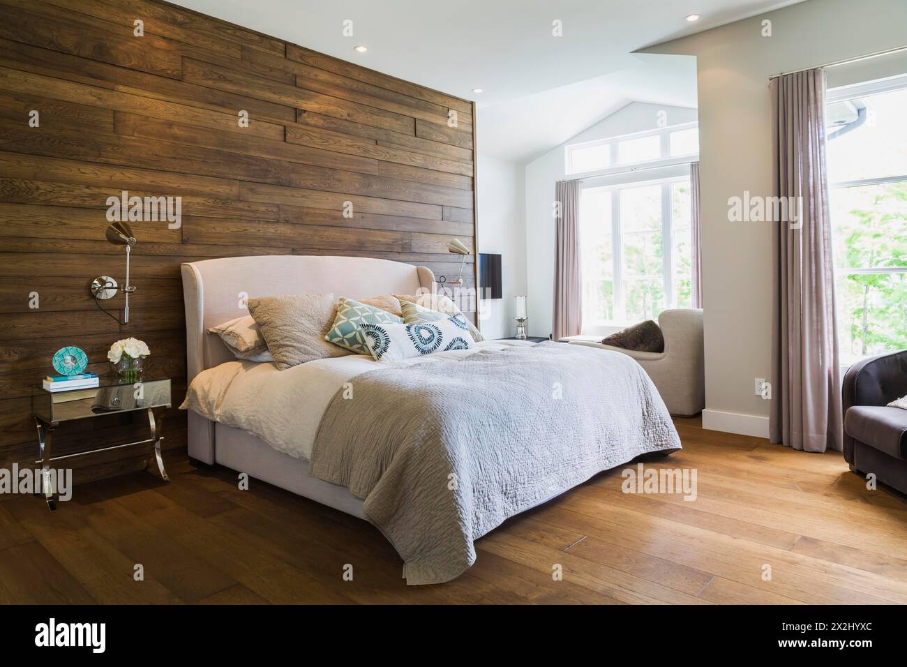Kingsize-Bett mit grauem Leinenkopfteil, Nachttisch aus Chrom und Spiegelglas im Hauptschlafzimmer mit Hickory-Holzdielen Stockfoto