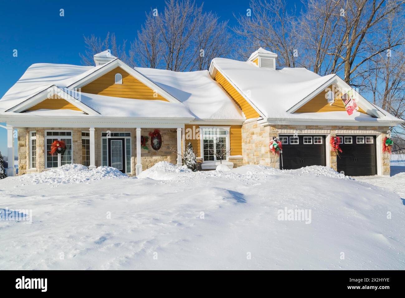 Beige und braune Naturstein mit gelber Holzverkleidung, weiße und schwarze Hausfassade im Landhausstil im Winter, Quebec, Kanada Stockfoto