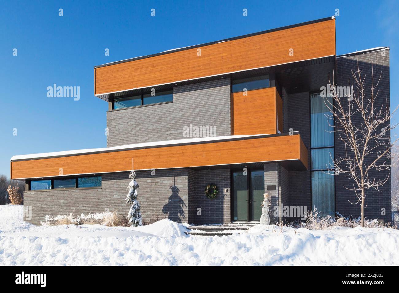 Moderne, graue Ziegelsteine und gebeizte Holzfassade im Cube-Stil mit schwarzer Zierleiste im Winter, Quebec, Kanada Stockfoto