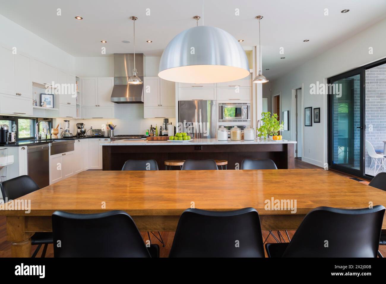 Offen gestalteter Ess- und Küchenbereich mit antikem Esstisch mit schwarzen Leder- und Kunststoffstühlen, Holzinsel mit Marmorplatte und schwarz lackiertem Holz Stockfoto