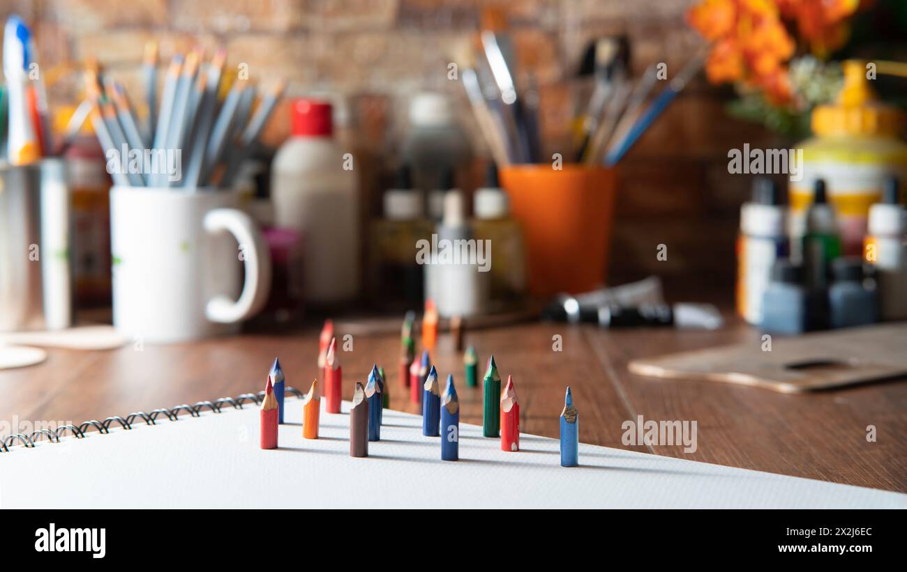 Kleine Buntstifte auf weißem Papier auf einem Holztisch mit Kunstzubehör im Hintergrund unscharf Stockfoto