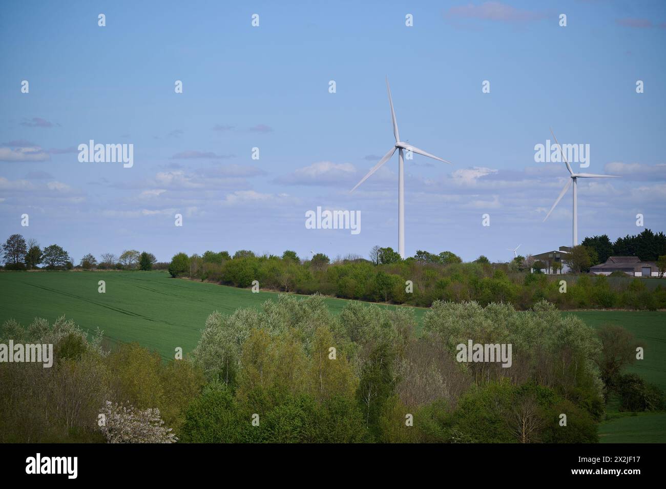 Zwei Windturbinen über englischer Landschaft vor blauem Himmel mit kleinen Wolken Stockfoto