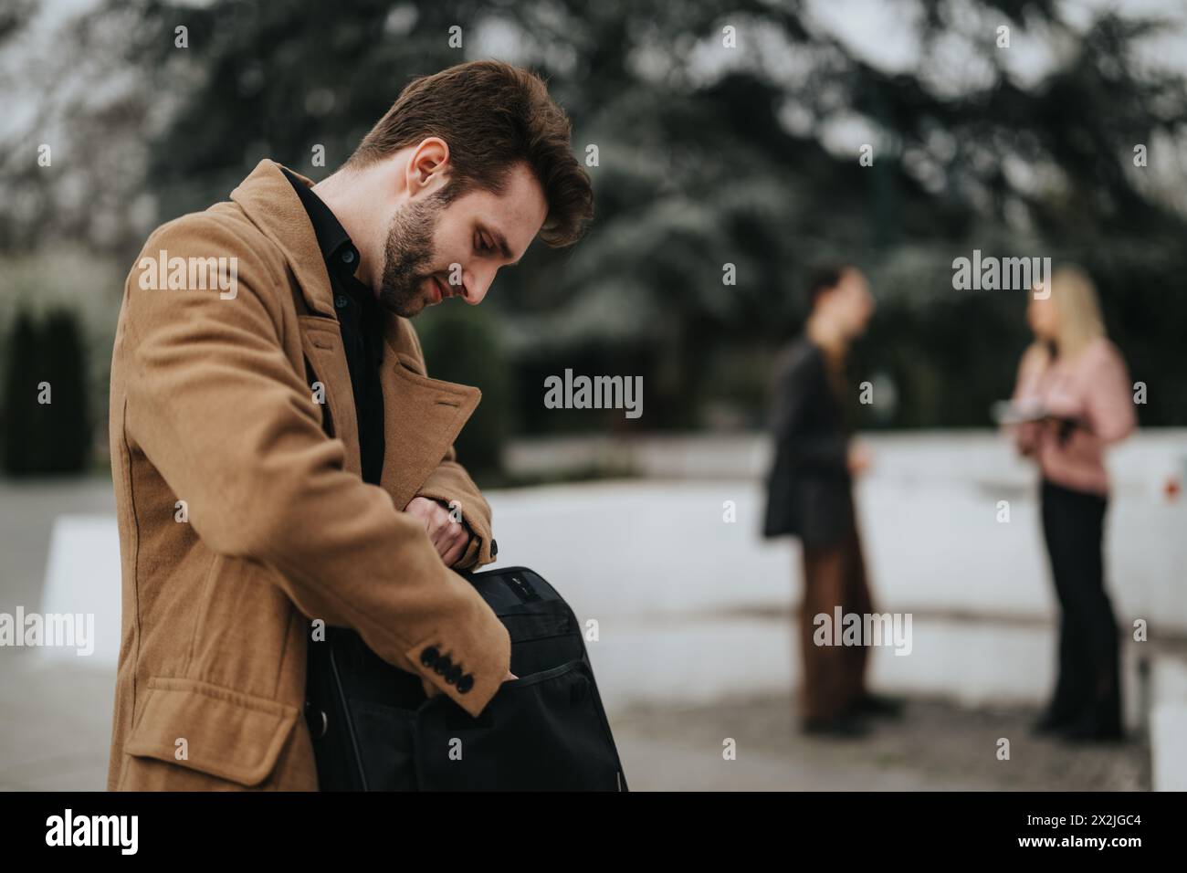 Zielgerichteter Geschäftsmann, der mit Kollegen im Hintergrund die Tasche überprüft Stockfoto