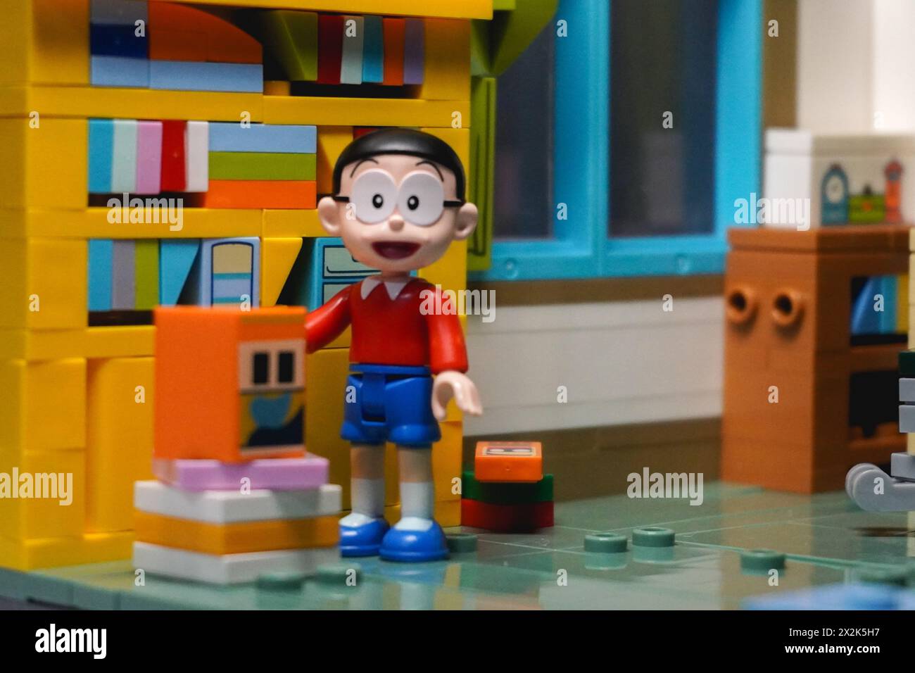 Nobitas Figur steht neben dem Bücherregal und dem Stapel Bücher in seinem Zimmer und lächelt Stockfoto