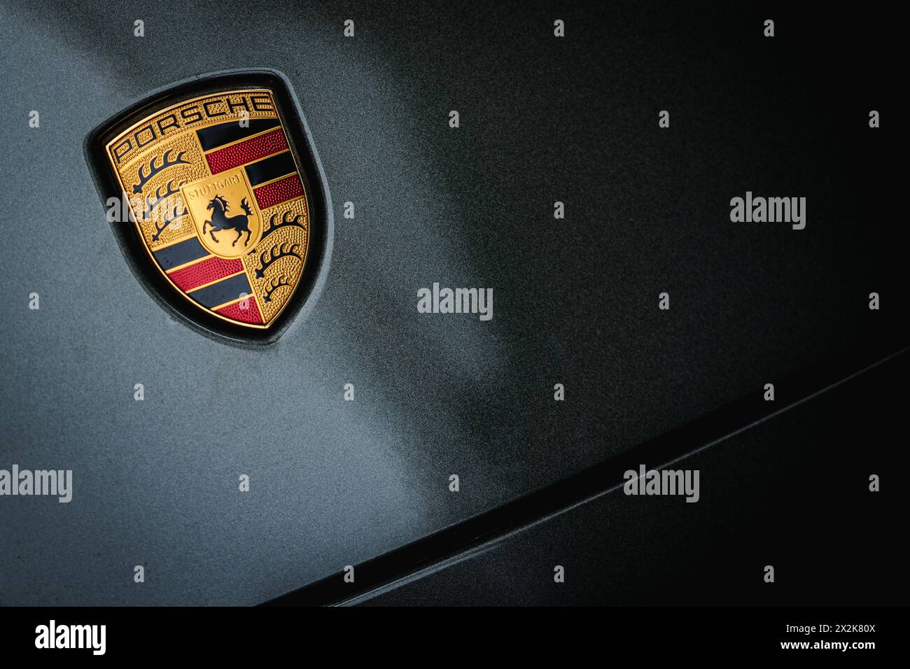 Nahaufnahme eines Luxuswagenemblems auf einer dunklen strukturierten Oberfläche, das Eleganz und Fahrzeugbranding zeigt. Graues Auto, Porsche-Logo-Emblem Stockfoto