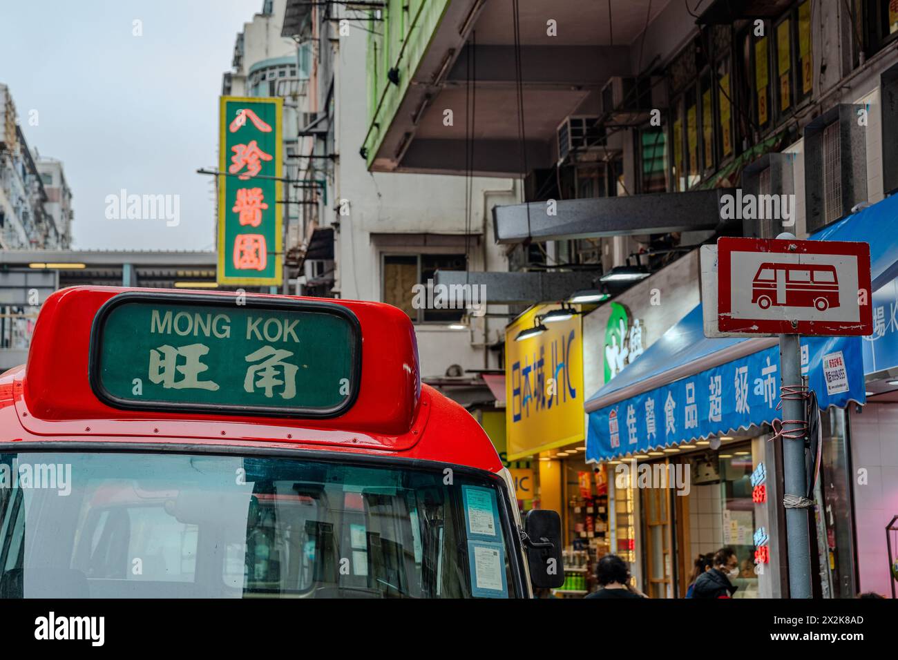 Pulsierende Straßenszene in Mong Kok, Hongkong, mit einer lebhaften Marktatmosphäre mit farbenfrohen Schildern und einem traditionellen roten Taxi, das deutlich hervorgehoben wird. Stockfoto