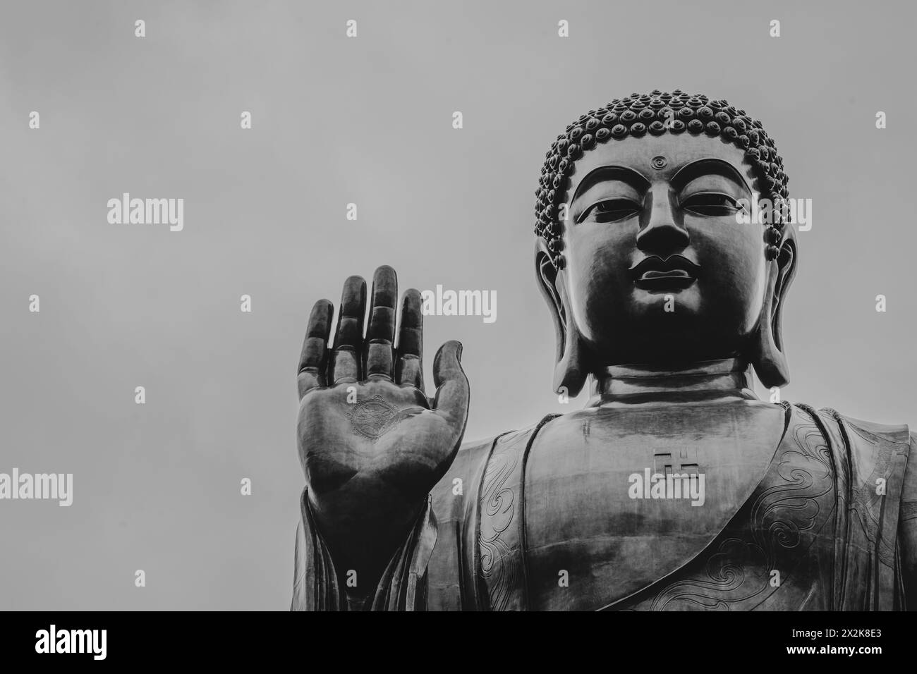 Ein Schwarzweiß-Bild mit einer großen Buddha-Statue, die einen ruhigen Ausdruck und eine erhobene Hand zeigt, vor einem klaren Himmel. Stockfoto