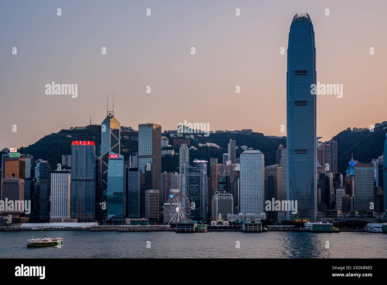 Ein ruhiger abendlicher Blick auf Hongkongs Stadtlandschaft mit Wolkenkratzern und einer Uferpromenade, aufgenommen bei Sonnenuntergang mit warmer Beleuchtung. Stockfoto