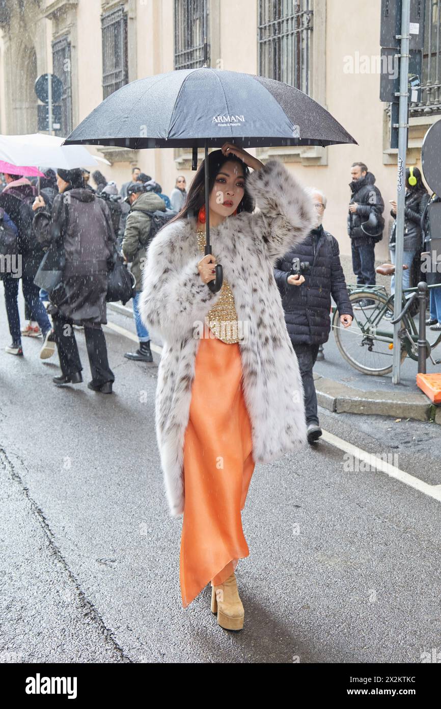 MAILAND, ITALIEN - 25. FEBRUAR 2024: Frau mit orangefarbenem Seidenkleid und weißem, grauem Pelzmantel vor der Modeschau Giorgio Armani, Mailand Fashion Week Street Stockfoto