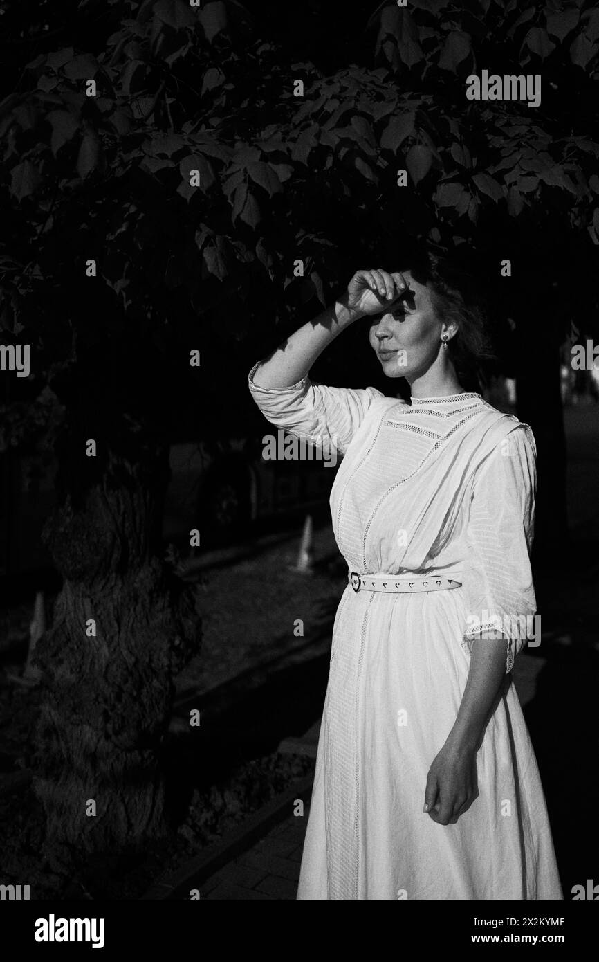 Eine elegante Frau mittleren Alters in einem weißen Vintage-Kleid vor dem Hintergrund historischer Gebäude im Morgenlicht Stockfoto