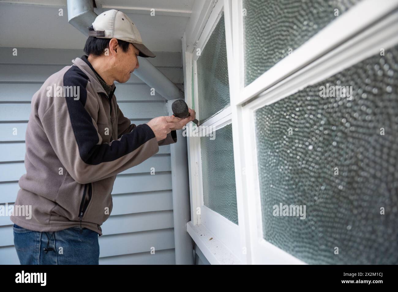 Arbeiter entfernen alten Fensterkitt mit Hammer und Meißel. Projekt zur Hauspflege. Stockfoto