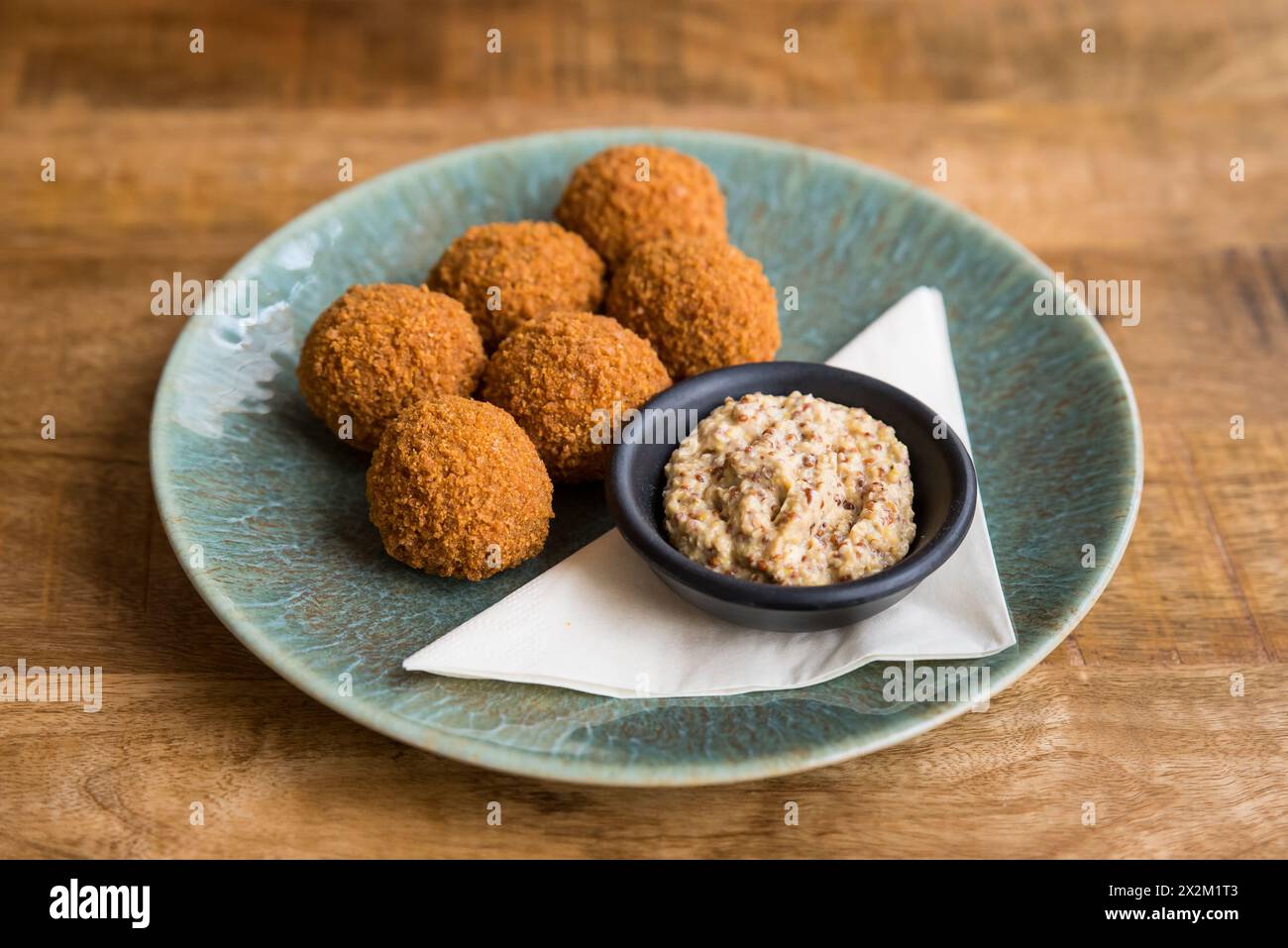 Nahaufnahme traditioneller niederländischer Bitterballen mit Senf auf einem Teller auf einem Holztisch Stockfoto