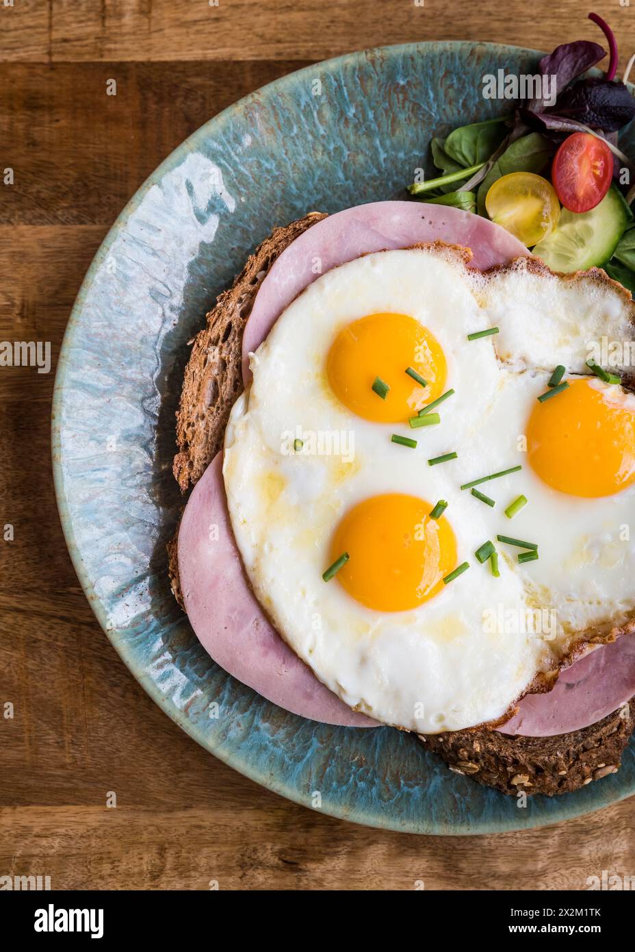 Blick von oben auf gebratene Eier und Schinken auf Brot auf einem Teller auf einem Holztisch im Café-Restaurant Stockfoto
