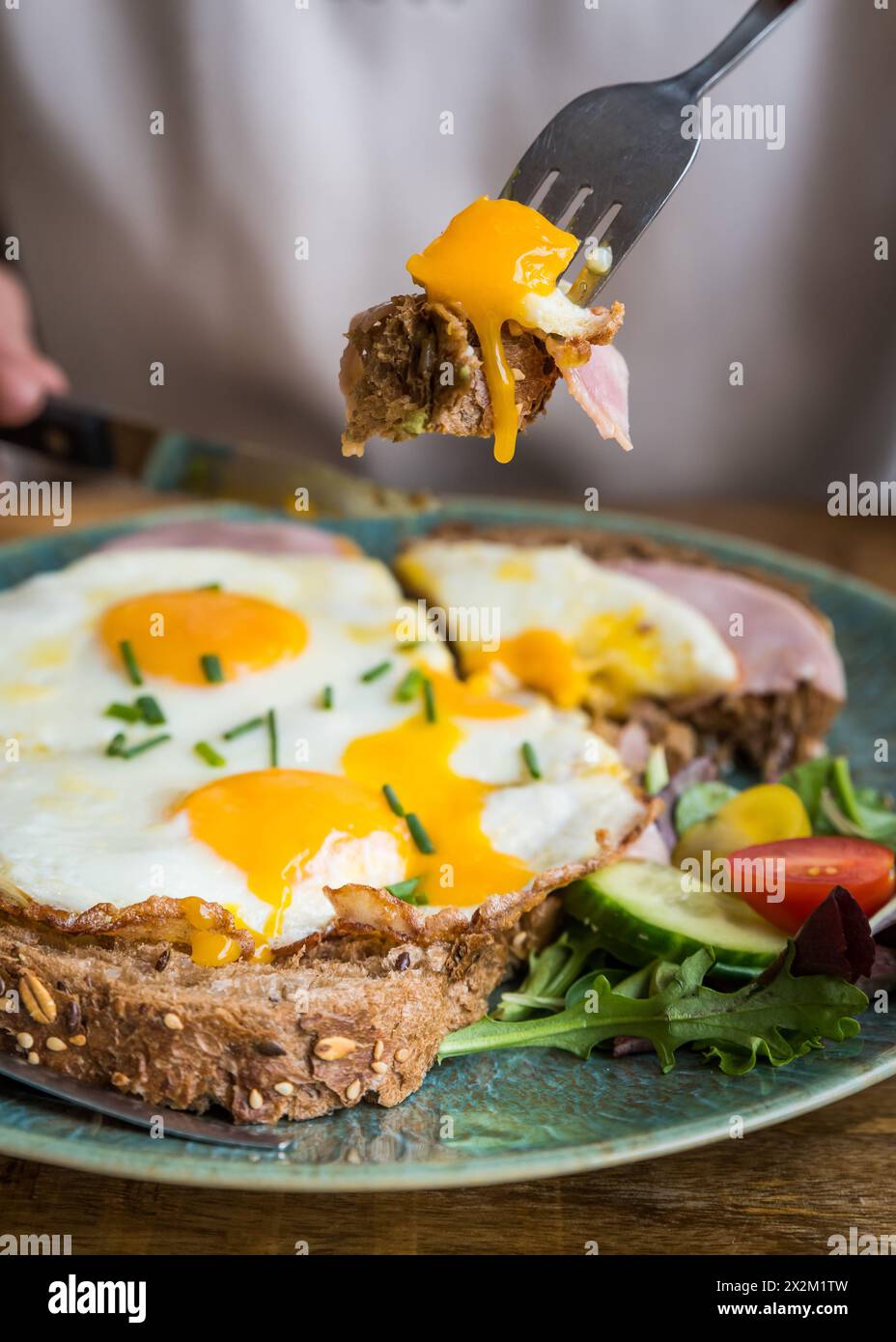 Nahaufnahme von Spiegeleiern und Schinken auf Brot auf einem Teller, die auf einem Holztisch im Café-Restaurant gegessen werden Stockfoto