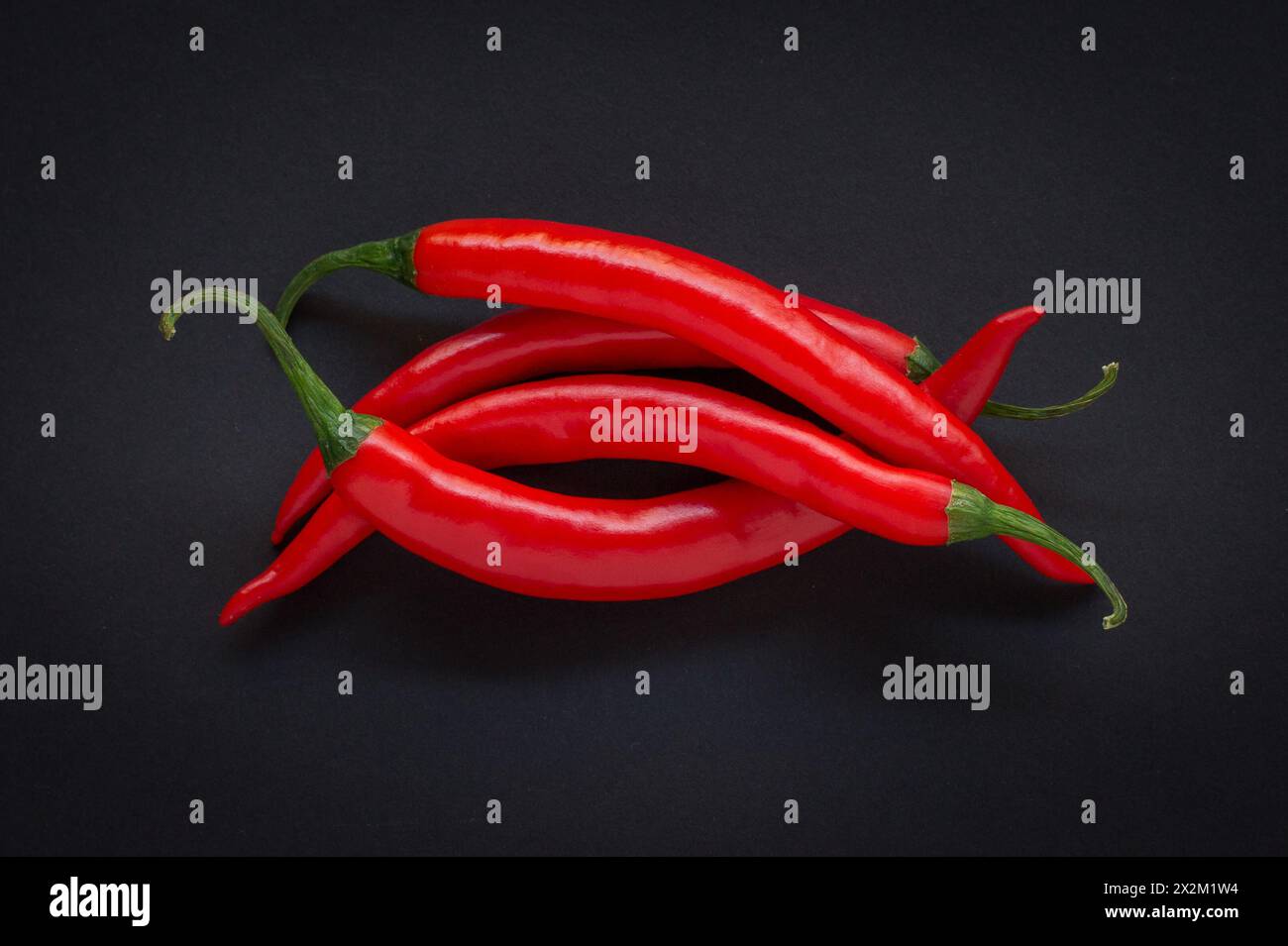 Frische rote Chili-Paprika auf einem Stapel auf schwarzem Hintergrund Stockfoto