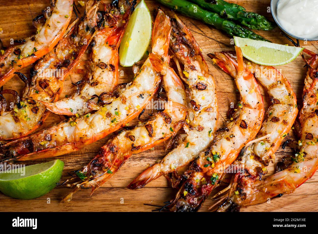 Blick von oben auf gegrillte Garnelen mit Limetten, Spargel und Mayo auf Holzbrett Stockfoto