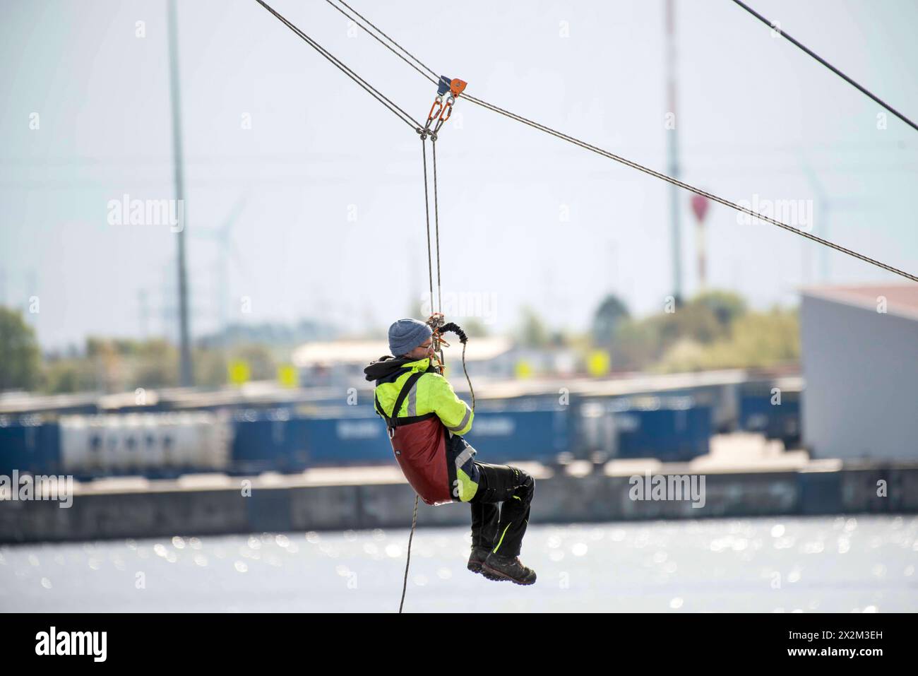 Eine Person wird von Höhenretter der Berufsfeuerwehr Rostock von einem Mast der Wakeboardanlage in Rostock Schmarl gerettet. Vor der Kulisse des Überseehafens an der Warnow wird die Berufsfeuerwehr Rostock erstmals eine Übung in der Wassersportanlage durchführen. Das Szenario umfasst einen medizinischen Notfall bei einem Servicetechniker bei Wartungsarbeiten an einem der 13 Meter hohen Motormasten der Wakeboardanlage auf der Rostocker Warnow. Die Rettung des Mannes erfordert den Einsatz der Höhenretter, wobei die Herausforderung besteht, dass der Rettungspunkt direkt über dem Wasser liegt. Stockfoto