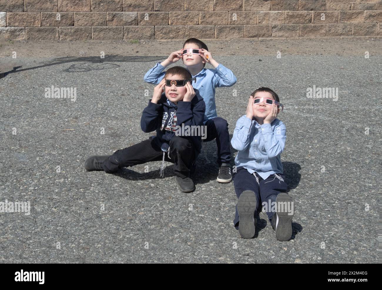 3 orthodoxe jüdische Kinder beobachten die Sonnenfinsternis von 2024 auf dem Schulhof ihrer Jeschiwa. Im Rockland County, New York. Stockfoto