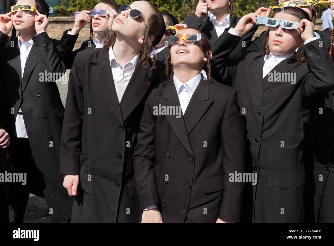 Eine Gruppe orthodoxer jüdischer Jeschiwa-Schüler mit langem Peyus beobachten die Sonnenfinsternis von 2024 auf ihrem Schulhof. Im Rockland County, New York. Stockfoto