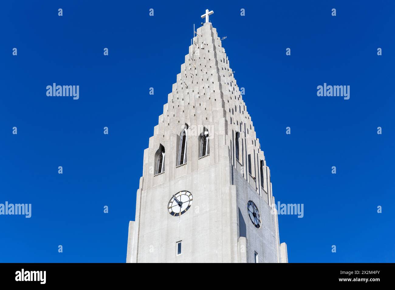 Hallgrimskirkja Kirchturm mit Heiligem Kreuz und Uhr, Reykjavik, Island, moderner Glockenturm vor klarem blauem Himmel. Stockfoto