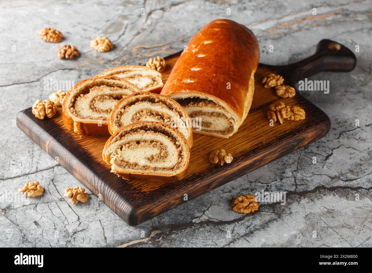 Festliche Nussrolle aus Hefeteig mit Walnüssen und Honig in Nahaufnahme auf einem Holzbrett auf dem Tisch. Horizontal Stockfoto