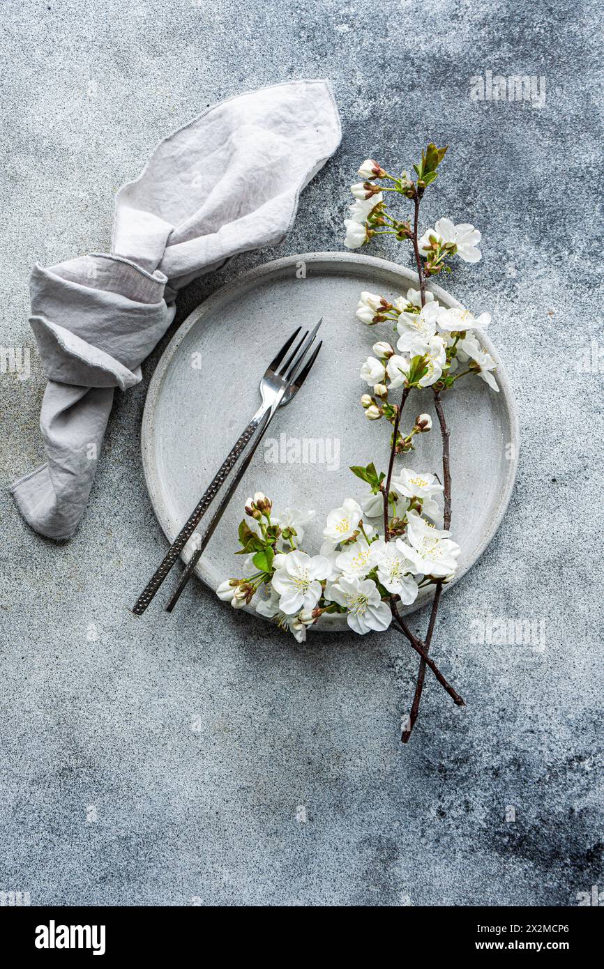 Ein eleganter Tisch mit Keramikplatte, Leinenserviette und Kirschblütenzweig, ideal für Frühlingsveranstaltungen oder Hochzeiten Stockfoto