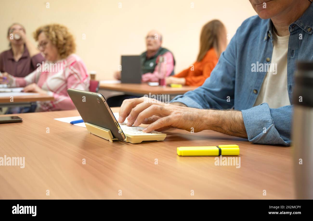 Ältere Schüler, die sich in einer Bildungsumgebung engagieren, konzentrieren sich auf einen Mann, der ein Tablet mit Kollegen im Hintergrund verwendet Stockfoto