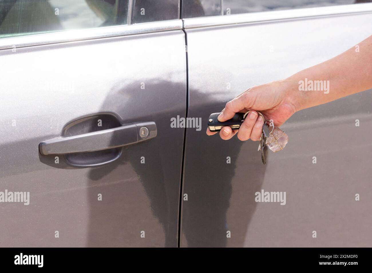 Eine Nahaufnahme einer Hand, die eine schlüssellose Entriegelungsfernbedienung hält, um eine moderne graue Autotür zu entriegeln Stockfoto