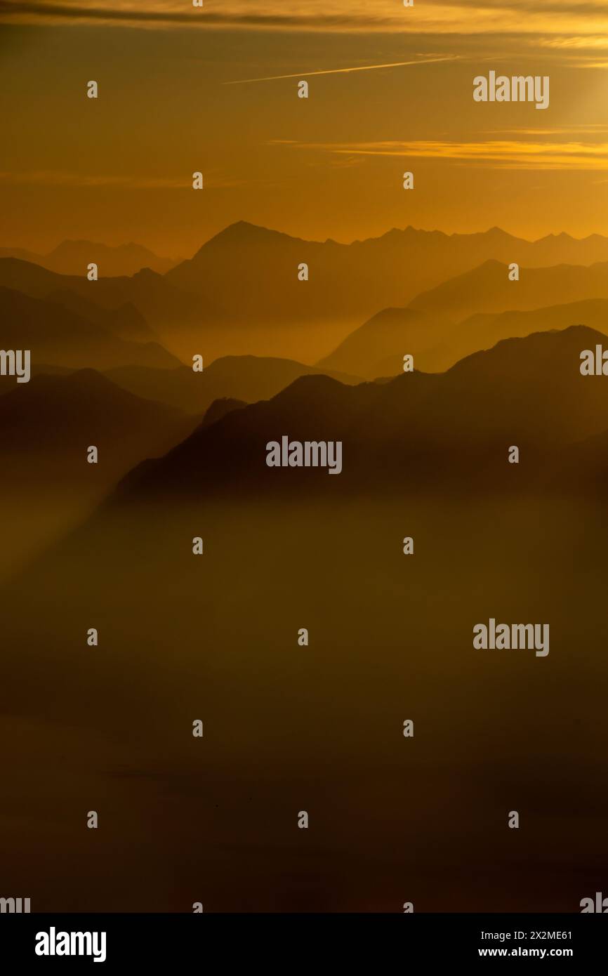 Ein ruhiger Blick auf die geschichteten Bergsilhouetten am Lago Maggiore während der goldenen Stunde, die eine mystische Atmosphäre schaffen Stockfoto