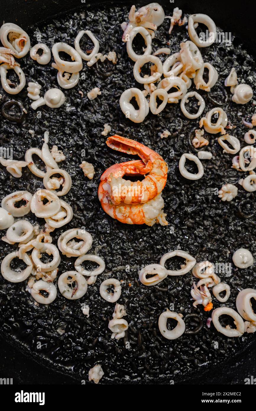 Blick von oben auf die traditionelle schwarze Reispassage, die mit Tintenfisch, Baby-Tintenfisch und Garnelen zubereitet wird, und zeigt den valencianischen Stil mit einem perfekten Sokarrat. Stockfoto