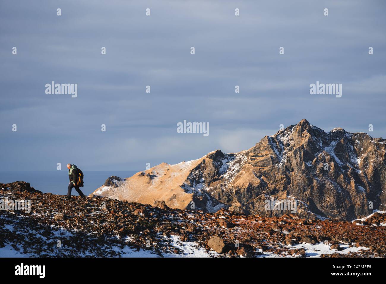 Ein einsamer Wanderer durchquert zerklüftetes Gelände in Island mit imposanten Bergen und einem dramatischen Himmel im Hintergrund Stockfoto