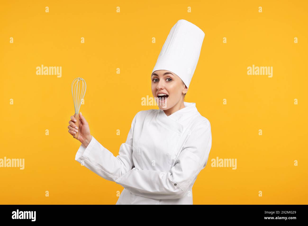 Überraschter professioneller Konditor in Uniform mit Schneebesen auf gelbem Hintergrund Stockfoto