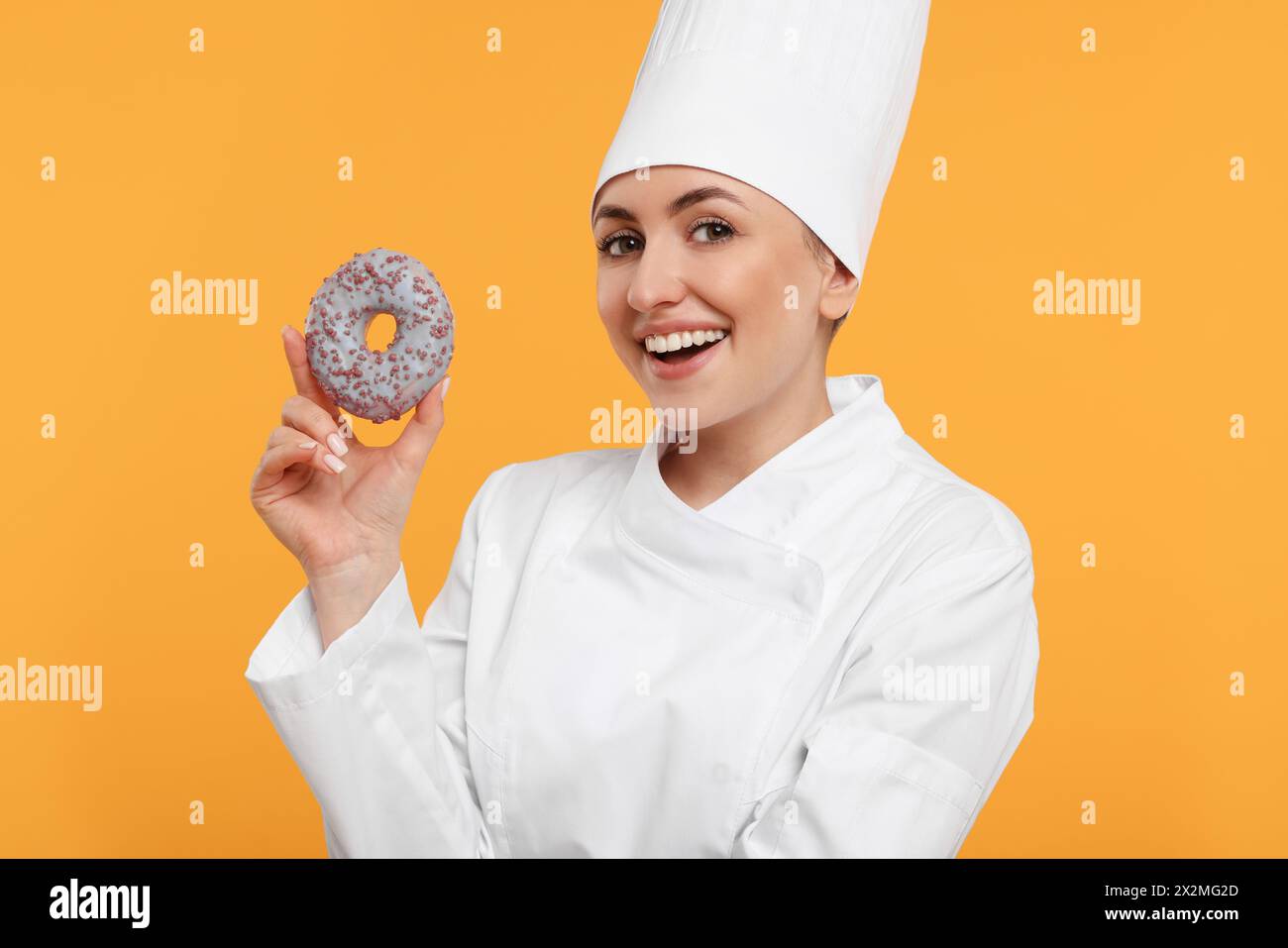 Glücklicher professioneller Konditor in Uniform mit köstlichem Donut auf gelbem Hintergrund Stockfoto