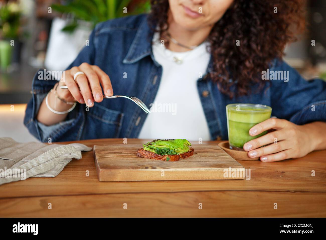 Frau genießt Avocado Toast und grünen Smoothie in einem Restaurant und bietet vegane gesunde Speisen. Stockfoto